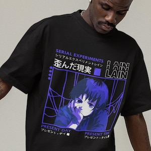 May include: Black t-shirt featuring a purple graphic of an anime character and text. The text includes "SERIAL EXPERIMENTS" and Japanese characters. The graphic is framed by a purple grid. The shirt is worn by a person.