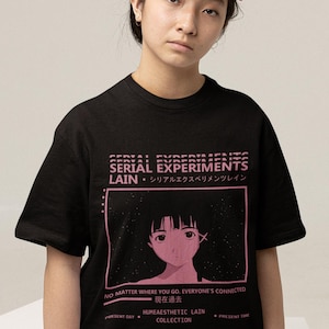 May include: Black t-shirt with pink text and graphic. The text reads "SERIAL EXPERIMENTS LAIN" in a stacked format, with Japanese characters below. A pink-framed image of a girl is centered below the text. Additional text includes "NO MATTER WHERE YOU GO. EVERYONE'S CONNECTED."