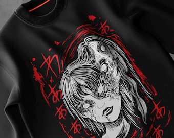 May include: Black sweatshirt featuring a graphic illustration of a woman with a partially decayed face, white eyes, and long hair. The design includes red accents and Japanese characters. The overall theme is horror.