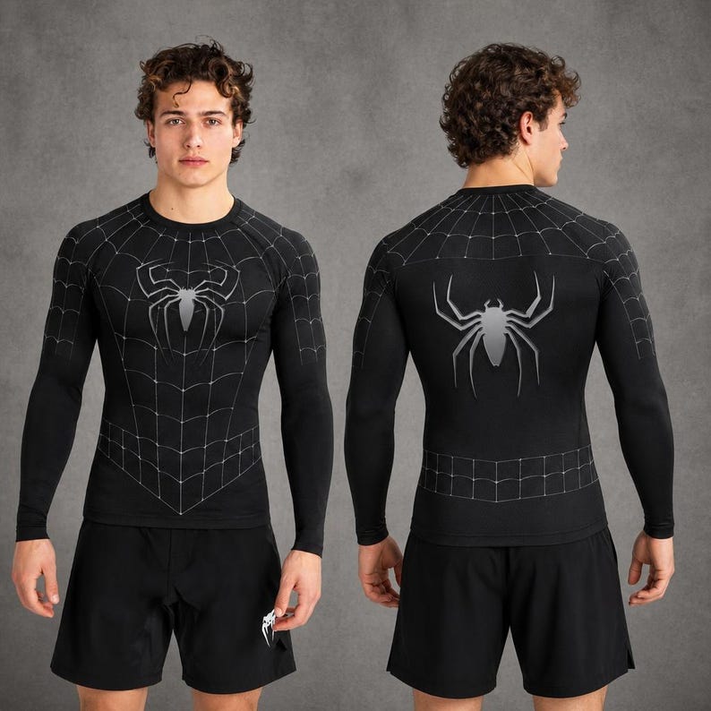 May include: A black long-sleeve compression shirt featuring a white spider web pattern across the chest and shoulders, with a large silver spider graphic centred on the front and back, paired with plain black athletic shorts.