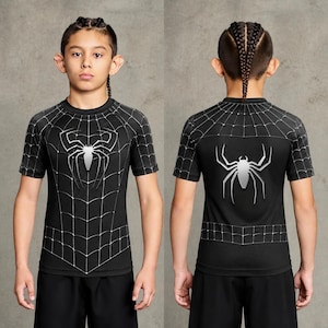 May include: A black short-sleeved athletic shirt featuring a white spider web pattern across the chest and shoulders, with a large silver spider emblem centred on the front and back. The garment is shown from both the front and back views.