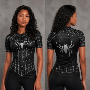 May include: A black short-sleeved athletic shirt featuring a white spiderweb pattern across the chest and shoulders, with a large silver spider emblem centred on the front and back. The fabric has a textured, honeycomb-like finish throughout.