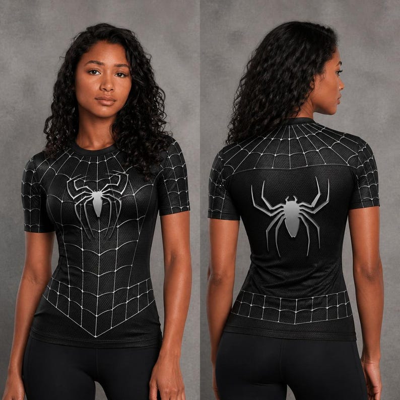 May include: A black short-sleeved athletic shirt featuring a white spiderweb pattern across the chest and shoulders, with a large silver spider emblem centred on the front and back. The fabric has a textured, honeycomb-like finish throughout.