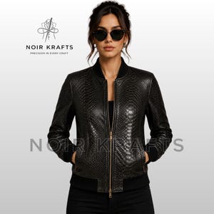 Könnte beinhalten: Schwarze Leder-Bomberjacke mit Schlangenleder-Textur, Reißverschluss vorne und schwarzen gerippten Bündchen und Saum. Die Jacke hat zwei Vordertaschen. Der Markenname "NOIR KRAFTS" ist sichtbar.