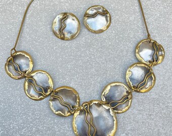 Puede incluir: Un collar de oro con un colgante de plata y oro. El colgante está hecho de varias piezas redondas conectadas entre sí. El collar también viene con un par de pendientes a juego.
