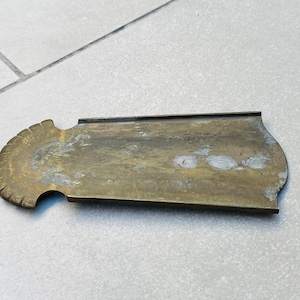 May include: A brass plate with a decorative scalloped edge. The plate is slightly tarnished and has a worn appearance.