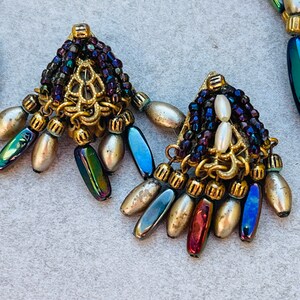 May include: A pair of gold tone earrings with iridescent blue and purple beads, white pearls, and a gold filigree design.