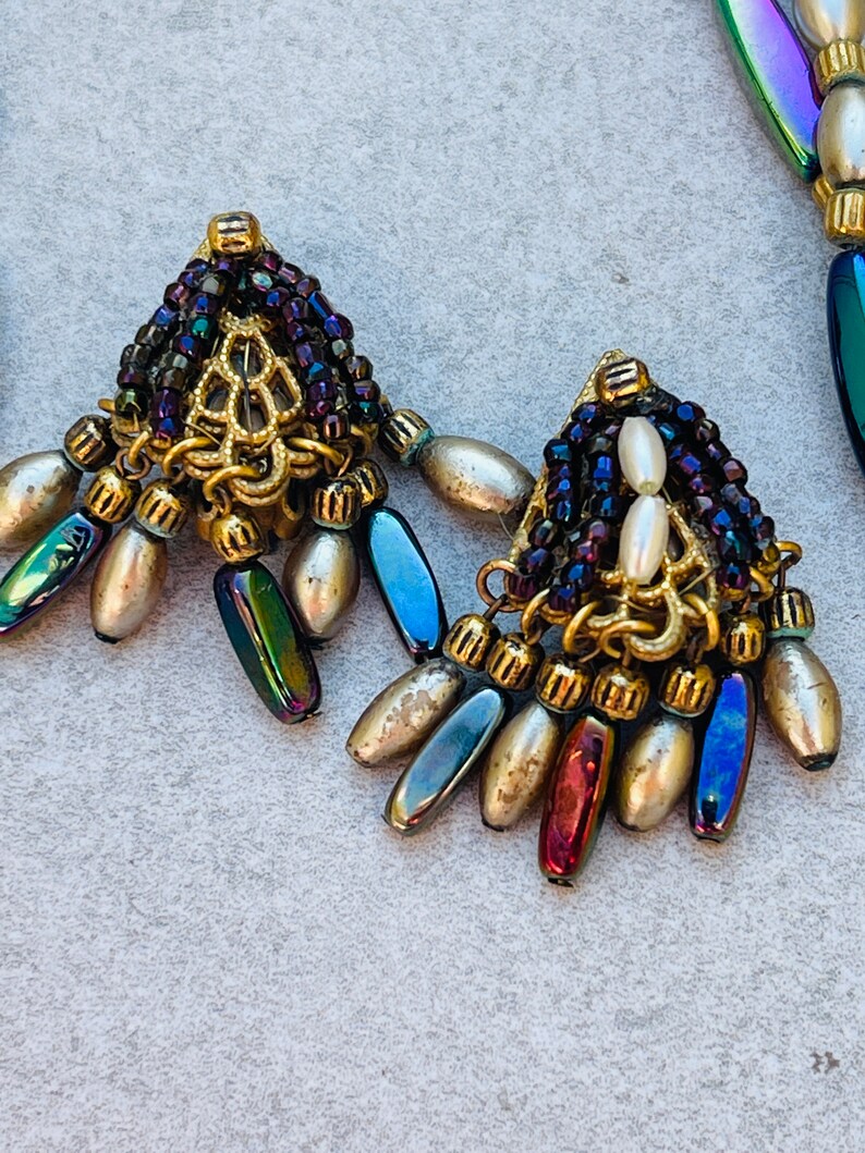 May include: A pair of gold tone earrings with iridescent blue and purple beads, white pearls, and a gold filigree design.