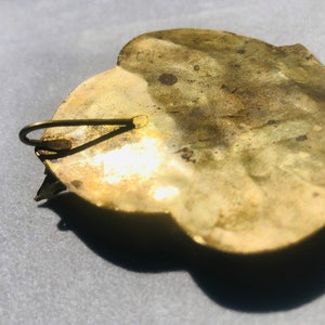 May include: A gold-toned metal brooch with a heart-shaped design. The brooch has a hook closure on the back.