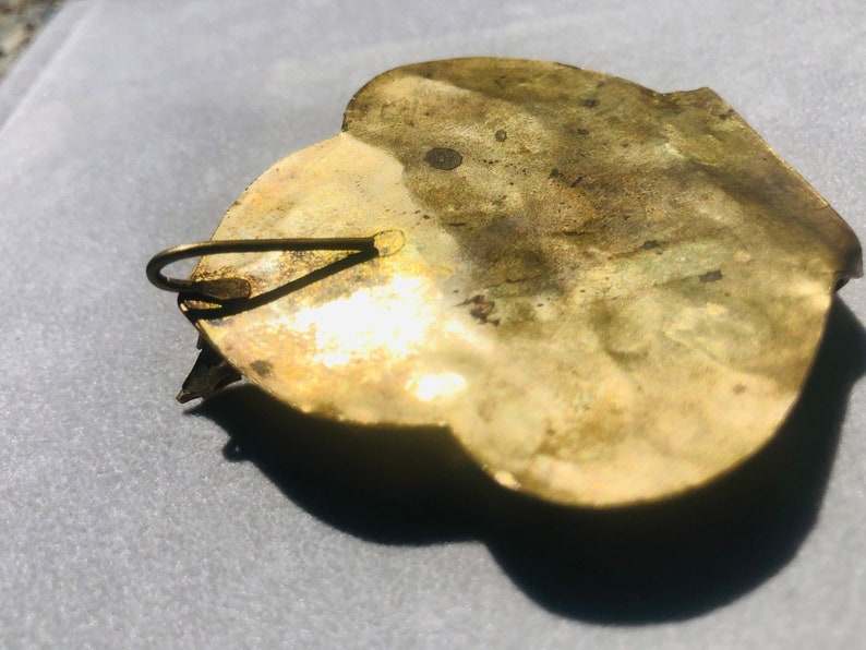 May include: A gold-toned metal brooch with a heart-shaped design. The brooch has a hook closure on the back.