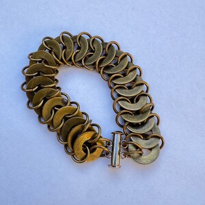 May include: A gold-toned bracelet made of interlocking metal rings. The bracelet has a simple, silver-toned clasp.