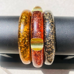 以下が含まれることがあります： 金色の斑点のあるバングルブレスレット3本。ブレスレットは琥珀色、赤色、黒色です。