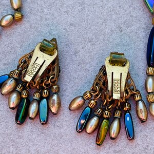 May include: A pair of gold tone earrings with iridescent blue and green beads and a gold tone 'Hob&eacute;' logo on the back of each earring.