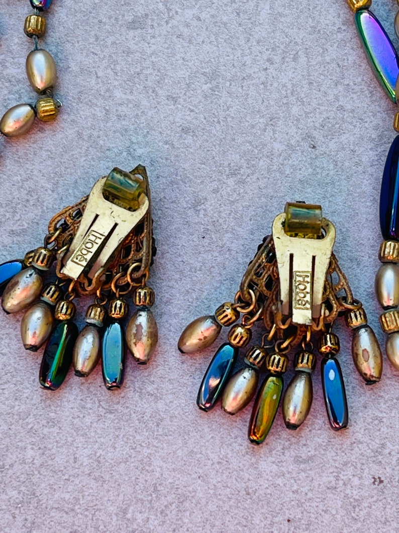 May include: A pair of gold tone earrings with iridescent blue and green beads and a gold tone 'Hob&eacute;' logo on the back of each earring.