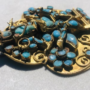 May include: A gold-toned pendant with a heart-shaped design, featuring intricate scrollwork and numerous turquoise stones.