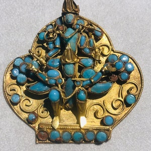 May include: A gold pendant with a turquoise blue deity figure in the center. The pendant is decorated with intricate gold filigree and turquoise blue stones.