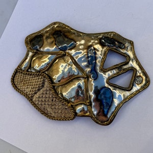 Może przedstawiać: Srebrna i złota broszka metalowa z fakturowaną powierzchnią i detalem ze skóry węża.