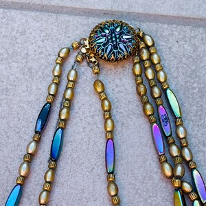May include: A multi-strand necklace with gold and iridescent beads. The necklace has a decorative clasp with a floral design.