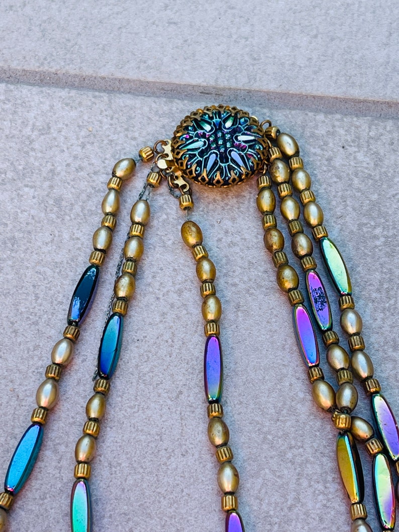 May include: A multi-strand necklace with gold and iridescent beads. The necklace has a decorative clasp with a floral design.