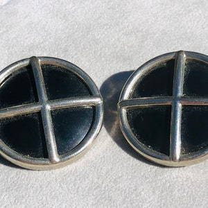 May include: A pair of silver tone earrings with black round cabochon stones. The stones are set in a silver frame with a cross design.