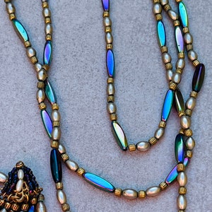 May include: A multi-strand necklace with iridescent oval beads and small white pearl beads. The necklace has a small pendant with iridescent oval beads and white pearl beads.