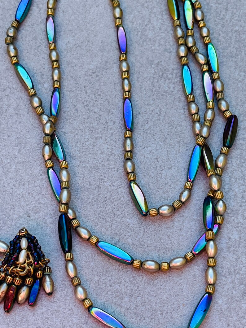 May include: A multi-strand necklace with iridescent oval beads and small white pearl beads. The necklace has a small pendant with iridescent oval beads and white pearl beads.