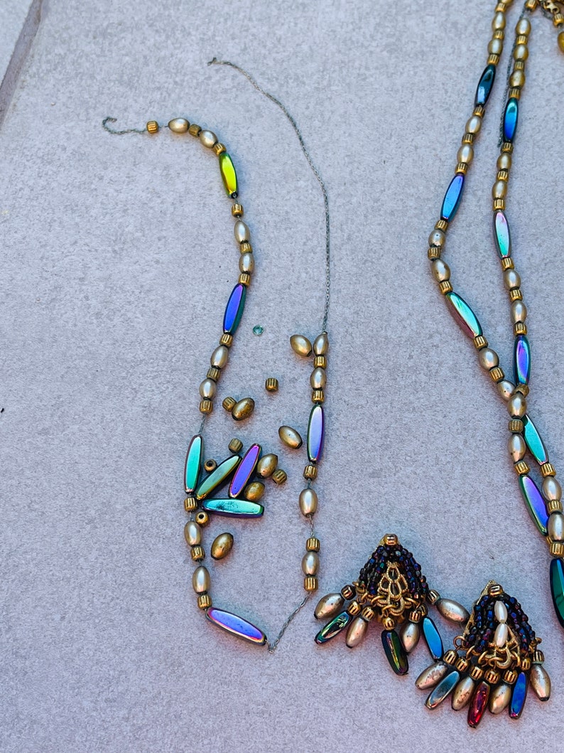 May include: Two strands of iridescent bead necklaces with gold accents and pearl-like beads. The necklaces are partially strung and have loose beads scattered around them. The necklaces have decorative tassels with iridescent beads and gold accents.