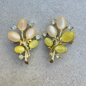 Puede incluir: Un par de pendientes dorados vintage. Cada pendiente presenta un diseño floral con piedras cabujón ovaladas de color amarillo pálido y amarillo. Pequeños cristales transparentes añaden brillo.