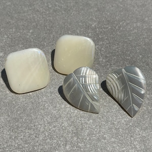 May include: Three white mother-of-pearl earrings. Two are square shaped and one is a leaf shape.