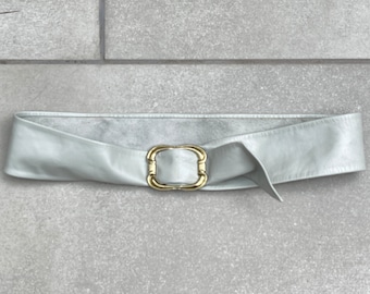 May include: A light gray leather belt with a gold-toned buckle. The buckle is a simple square shape with rounded edges.