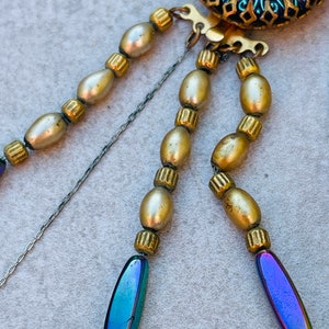 May include: A multi-strand necklace with gold and iridescent blue beads. The necklace has a decorative clasp with a blue and green enamel design.