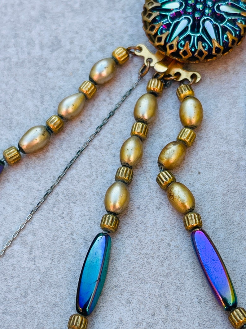 May include: A multi-strand necklace with gold and iridescent blue beads. The necklace has a decorative clasp with a blue and green enamel design.