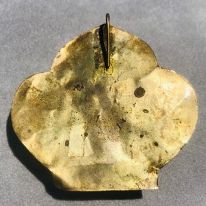 May include: A gold-colored metal pendant in the shape of a stylized flower with a loop at the top for hanging.