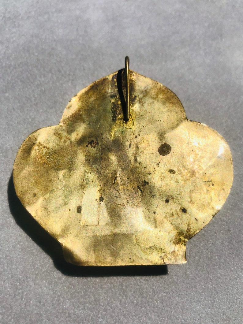 May include: A gold-colored metal pendant in the shape of a stylized flower with a loop at the top for hanging.