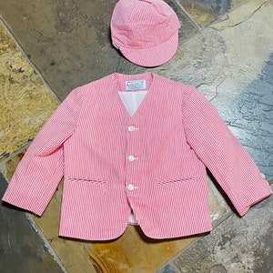 Puede incluir: Una chaqueta de rayas rojas y blancas con cierre de botones y mangas largas. También se incluye una gorra a juego de rayas rojas y blancas.