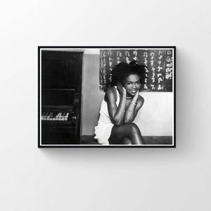 May include: Monochrome photograph of a woman in a white dress, seated with her hands near her face. A piano is visible on the left, and a wall with script is behind her. The image is framed in a black border.