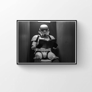 Può includere: Stampa in bianco e nero incorniciata di uno Stormtrooper di Star Wars che legge un libro. Lo Stormtrooper, con armatura e casco bianchi, è seduto in uno spazio poco illuminato.