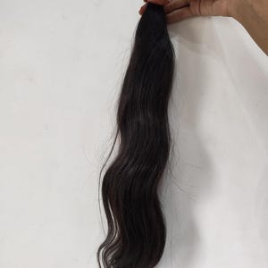 May include: A bundle of dark brown hair, held together with a red band. The hair is long, wavy, and appears to be unprocessed. The hair is against a white background.