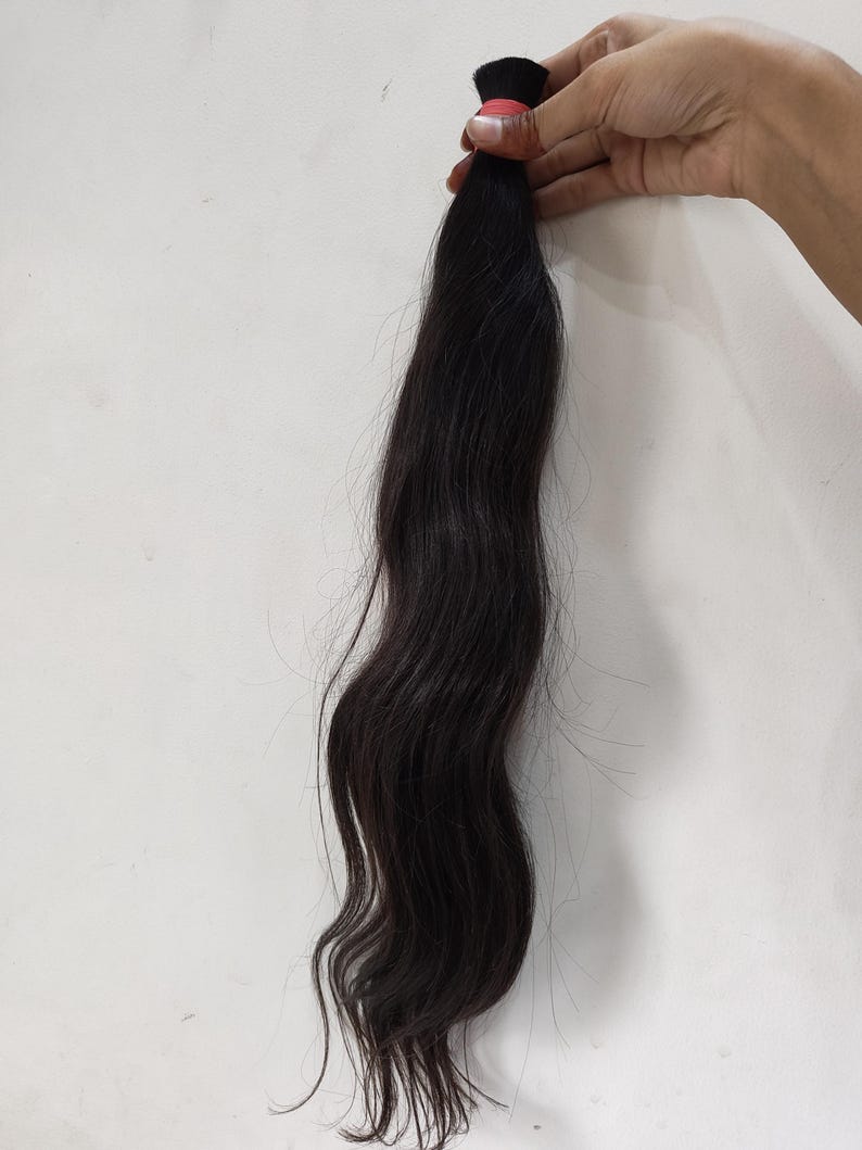 May include: A bundle of dark brown hair, held together with a red band. The hair is long, wavy, and appears to be unprocessed. The hair is against a white background.