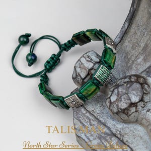May include: Green deluxe bracelet from the North Star Series. The bracelet features square green stones and silver accents. The adjustable cord is dark green. The word "TALISMAN" is visible in the image.