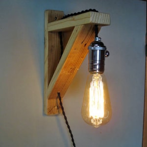 Op de afbeelding: Een houten wandlamp met een zwart snoer en een vintage-stijl gloeilamp. De lamp is gemaakt van gerecycled hout en heeft een rustieke uitstraling.