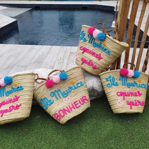 May include: Four straw tote bags with colorful pom-poms and embroidered text. The bags say "Ile Maurice" and "copines & ap&eacute;ro" in pink and blue lettering.