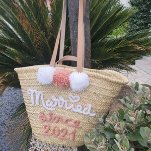 May include: A straw tote bag with white and pink pom poms and the text "Married since 2021" embroidered on the front.
