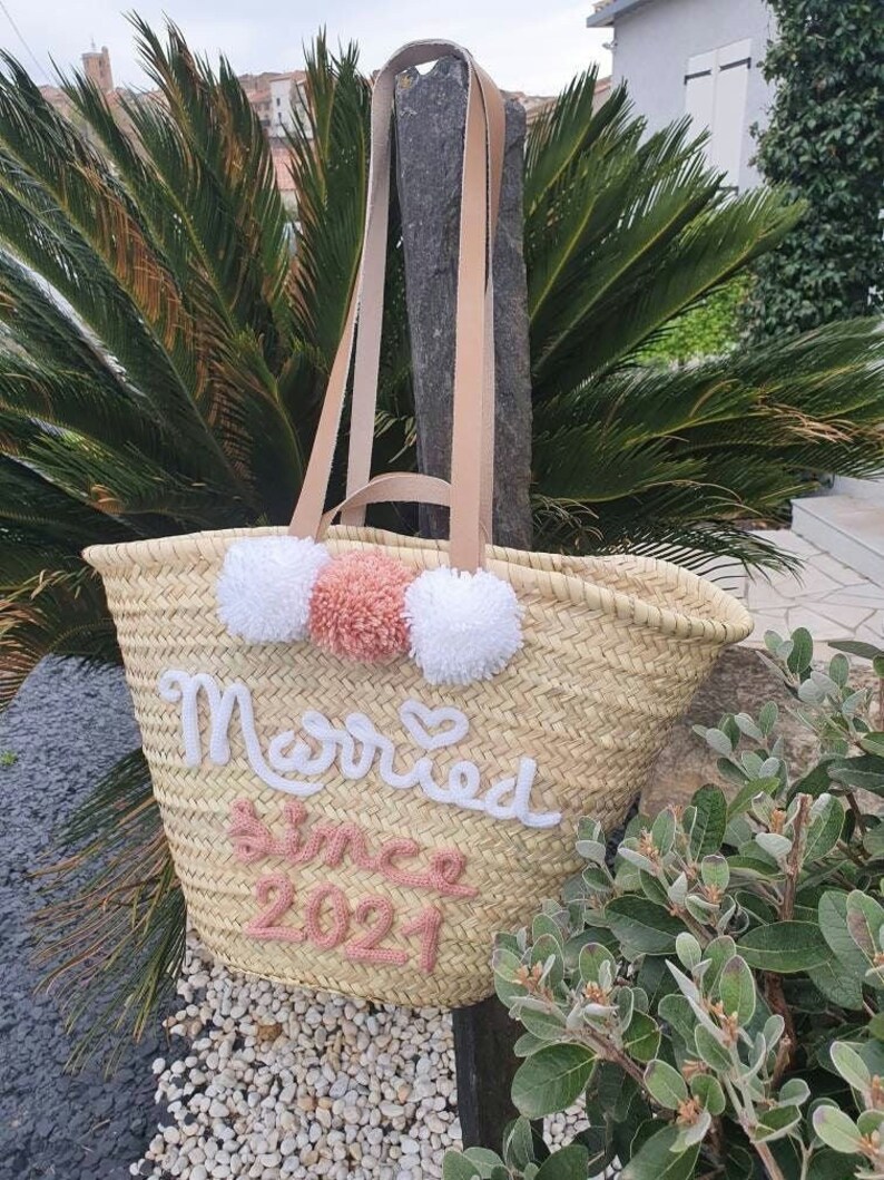 May include: A straw tote bag with white and pink pom poms and the text "Married since 2021" embroidered on the front.