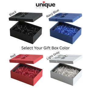 May include: Four rectangular gift boxes with lids, each featuring a textured surface, a decorative ribbon bow on top, and matching shredded paper filler inside. The boxes are available in black, navy blue, red, and light grey. Text reads: unique by melody, Select Your Gift Box Color, Black, Navy Blue, Red, Light Grey.