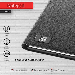 Può includere: Un blocco note nero con la scritta "Notepad" in un rettangolo rosso. Il blocco note è dotato di un supporto per telefono, incisione laser e batteria integrata. Il blocco note ha una piccola etichetta con la scritta "YOUR DESIGN L HERE".