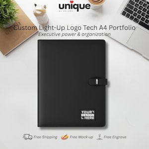 Può includere: Un portfolio A4 nero con un'area logo illuminata. Il portfolio ha una chiusura a scatto e il testo "YOUR DESIGN L HERE". La parte superiore dell'immagine presenta il testo "Custom Light-Up Logo Tech A4 Portfolio".