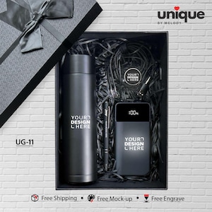 May include: A black gift box with a bow, containing a black tumbler, pen, power bank, and other accessories. The tumbler and power bank have the text "YOUR DESIGN L HERE". The power bank shows 100%. The box is labeled "UG-11".