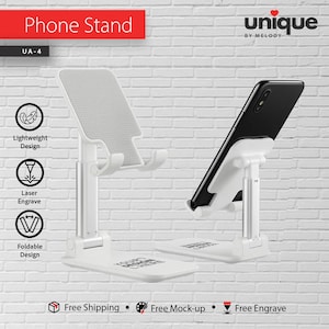 Może przedstawiać: Biały i srebrny stojak na telefon z telefonem na miejscu. Stojak jest regulowany i składany, ze słowami "Phone Stand" na czerwono u góry. Stojak ma lekką konstrukcję i jest grawerowany laserowo.