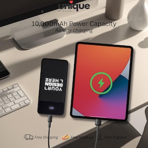 May include: A black rectangular power bank with a 10,000mAh capacity and a digital display showing 100 percent, connected via a black cable to a tablet displaying a green charging icon. The power bank features the white text DESIGN YOUR HERE.